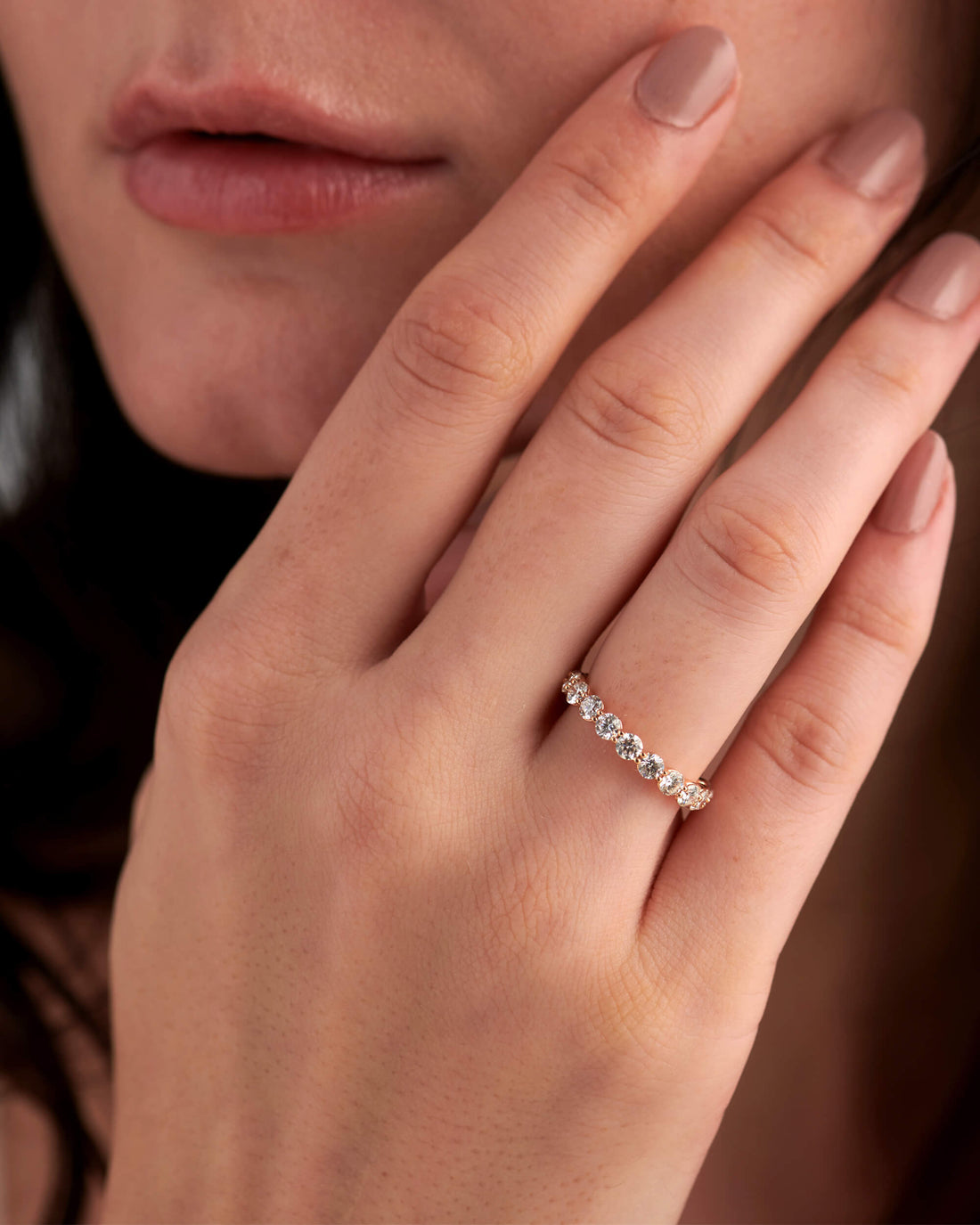 Round full eternity lab grown diamond wedding band in rose gold worn on a hand near the face