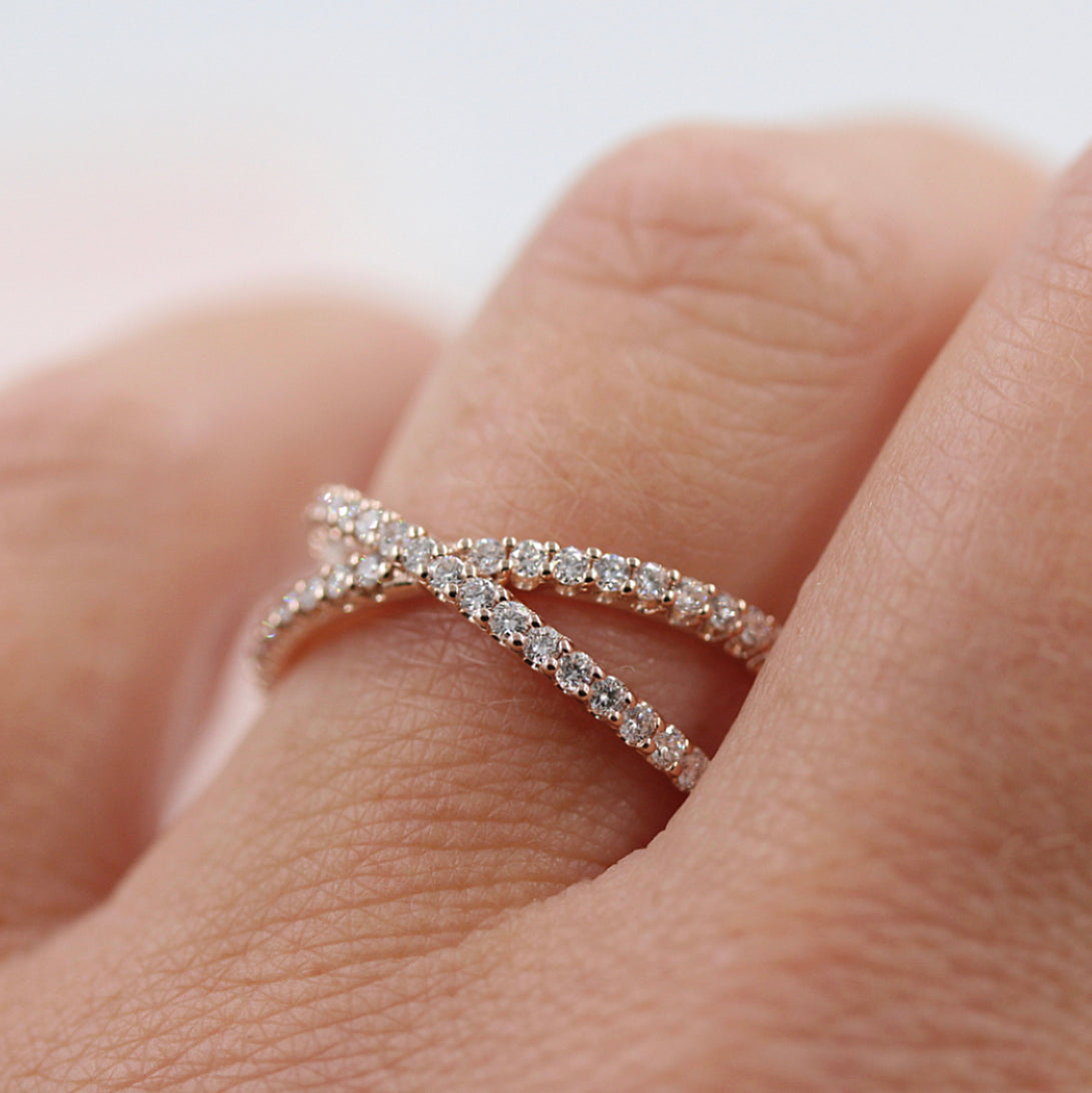 Round lab grown diamond criss cross wedding band in rose gold worn on a finger, close view