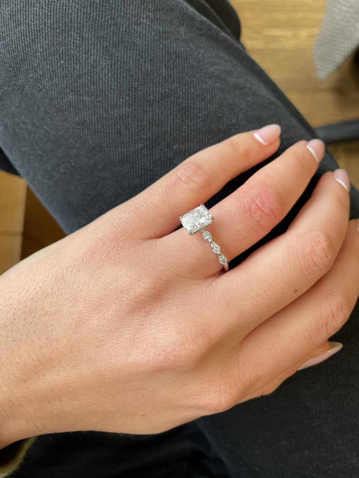 Cushion cut engagement ring with a marquise and round accent band worn on the hand