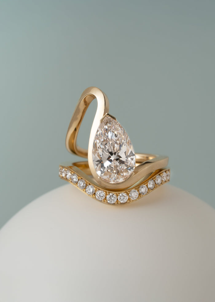 Pear cut lab grown diamond ribbon loop engagement ring shown with a curved pave band