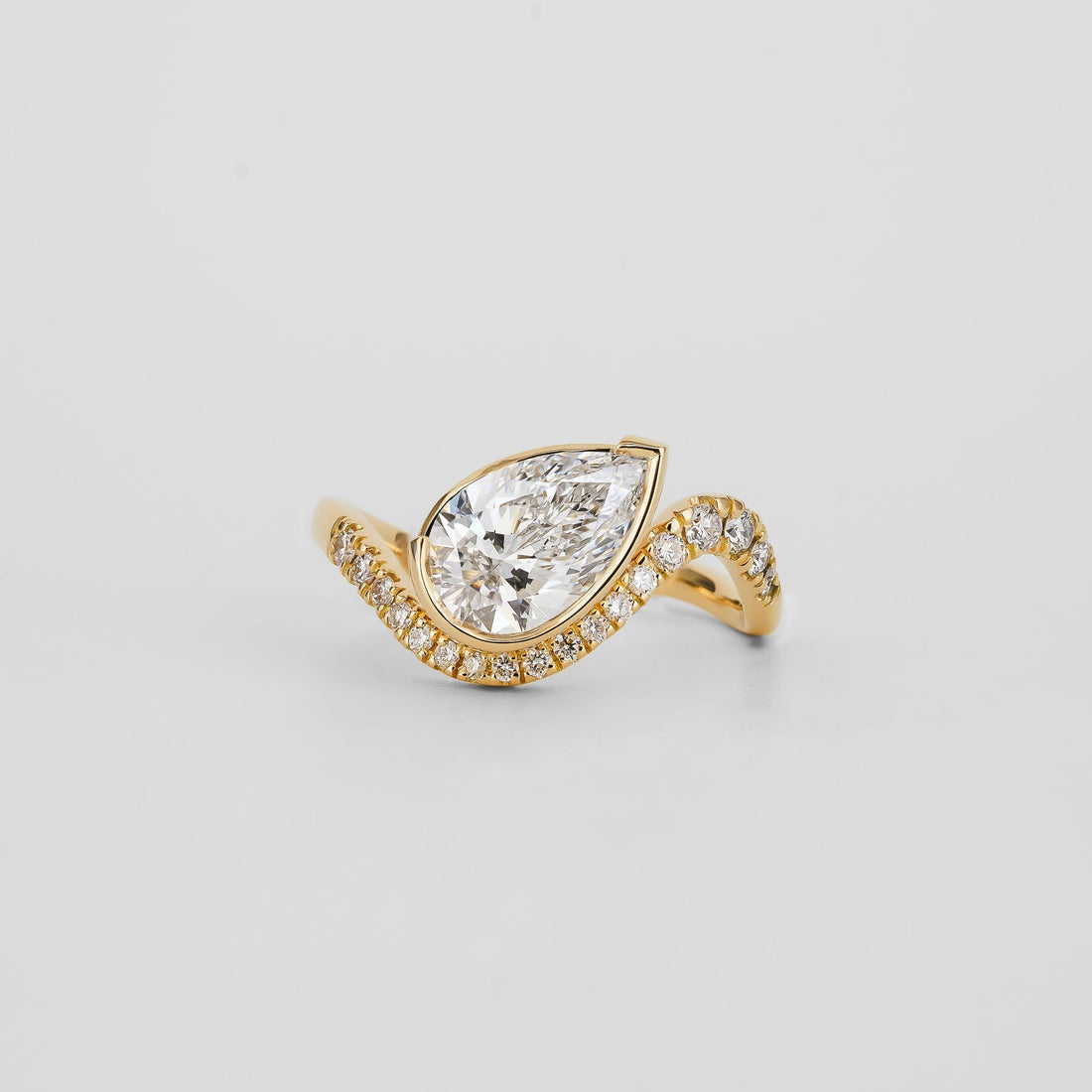 Pear cut lab grown diamond bezel ring on a twisted pave band in yellow gold