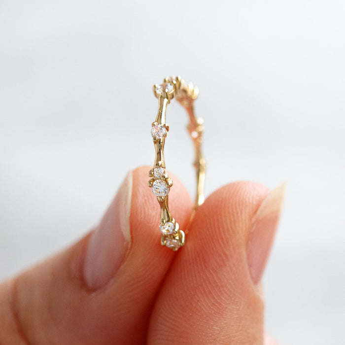 Yellow gold twig station moissanite band held upright between two fingers