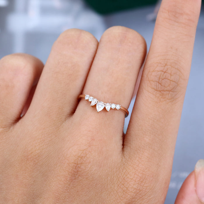 Round and pear moissanite curved wedding band in rose gold worn on the finger