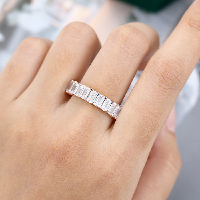 Emerald cut moissanite full eternity wedding band in rose gold worn on a finger
