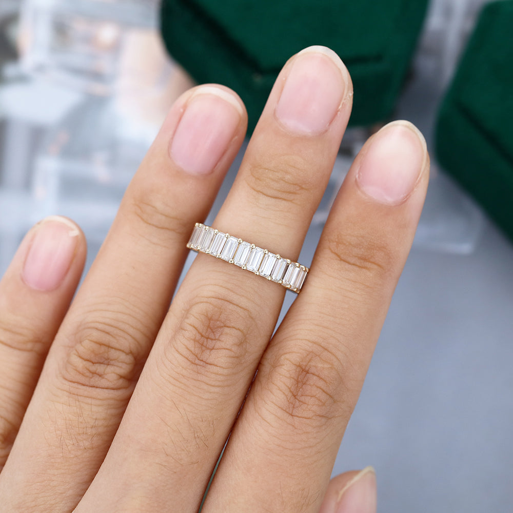 Emerald cut moissanite shared prong full eternity wedding band in yellow gold worn on the finger