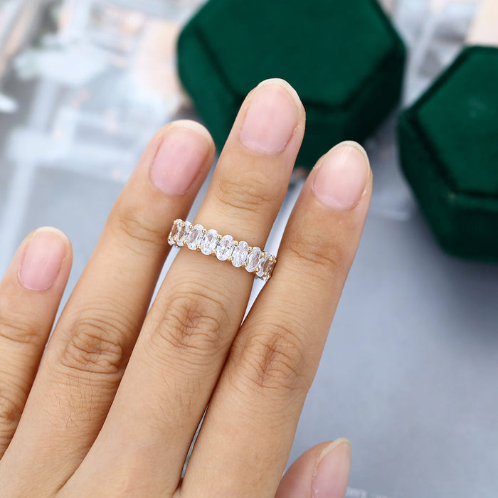 Oval moissanite prong set full eternity wedding band in yellow gold worn on the finger