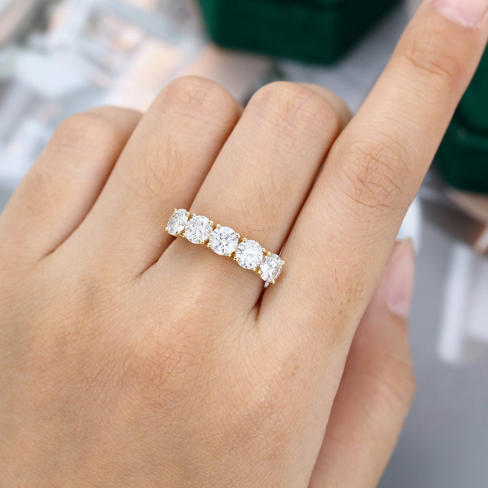 Round moissanite five stone wedding band in yellow gold worn on the finger