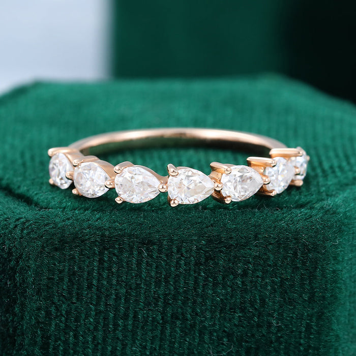 Front view of a rose gold half eternity band with pear shaped moissanite stones on green velvet