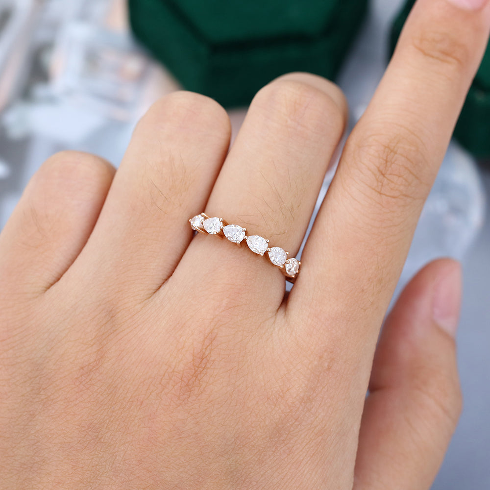 Pear moissanite prong half eternity wedding band in rose gold worn on a finger
