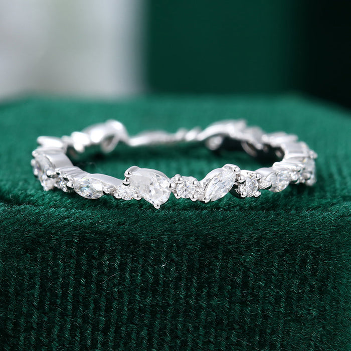 Front view of a full eternity band with marquise, round and pear moissanite stones on green velvet
