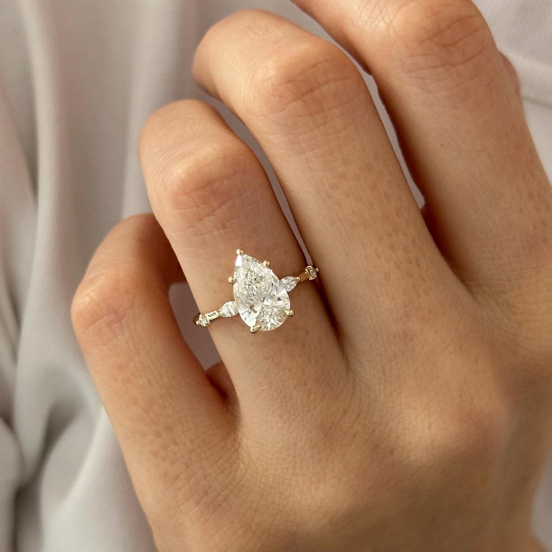 Pear cut lab grown diamond ring with marquise and round accents on a dainty band