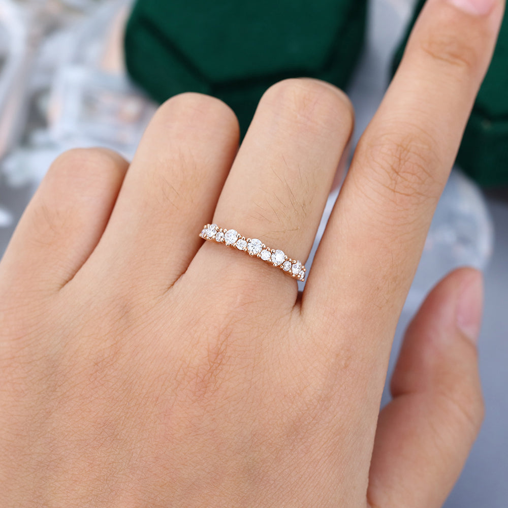 Round moissanite alternating size half eternity wedding band in rose gold worn on a finger