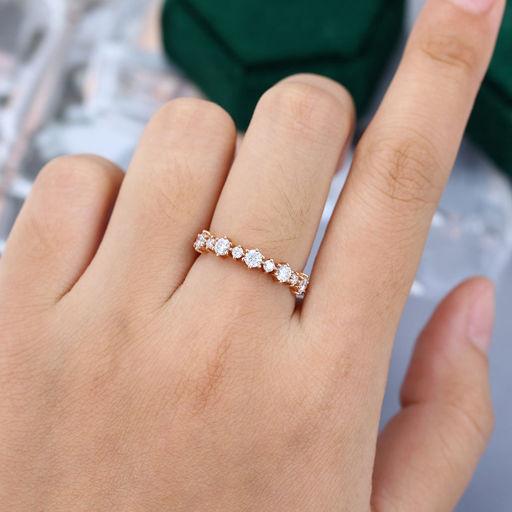 Round moissanite alternating size half eternity wedding band in rose gold worn on the finger