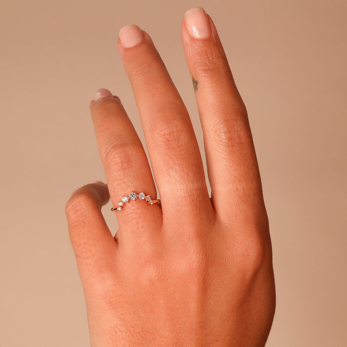 Round moissanite curved wedding band worn on a hand against a peach background