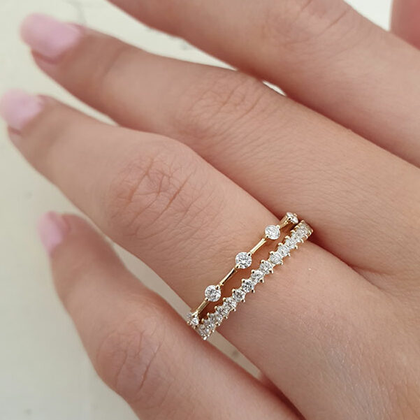 Dainty round lab grown diamond station band in yellow gold stacked with a diamond band on a hand