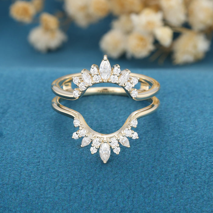Front view of a yellow gold double curved enhancer guard with marquise and round moissanite crowns on blue velvet