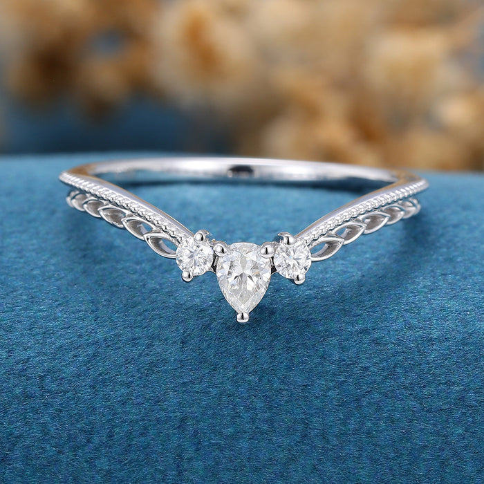 Front view of a white metal V shaped band with a pear and two round moissanite stones on blue velvet