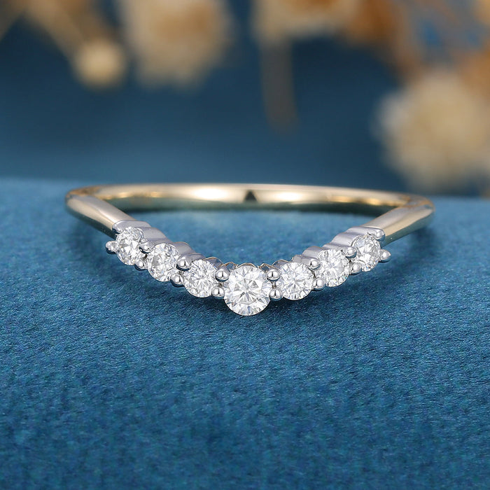 Front view of a curved wedding band with seven graduated round moissanite stones in yellow and white gold