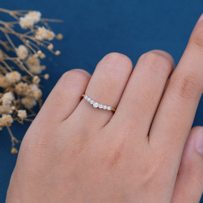 Round moissanite curved seven stone wedding band worn on a finger