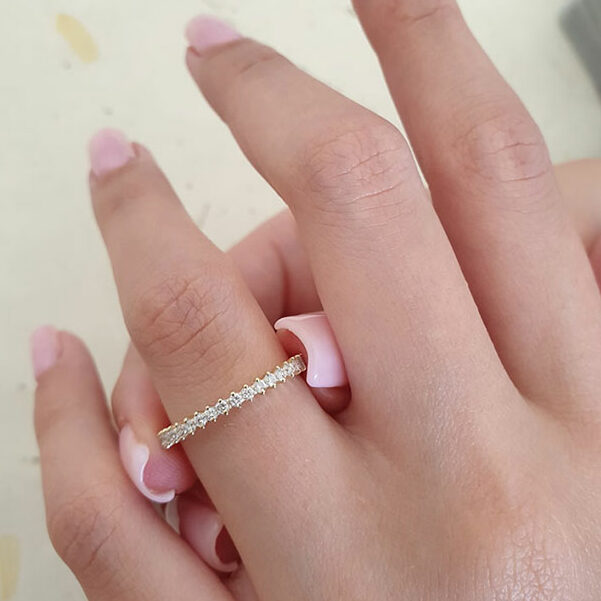 Slim round lab grown diamond half eternity wedding band in yellow gold worn on a finger