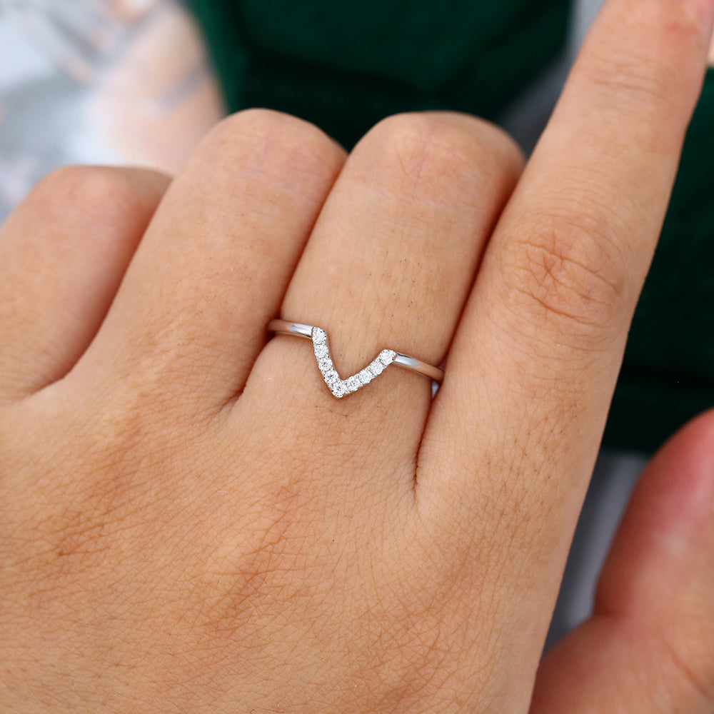 Round moissanite V-shaped curved wedding band worn on a finger