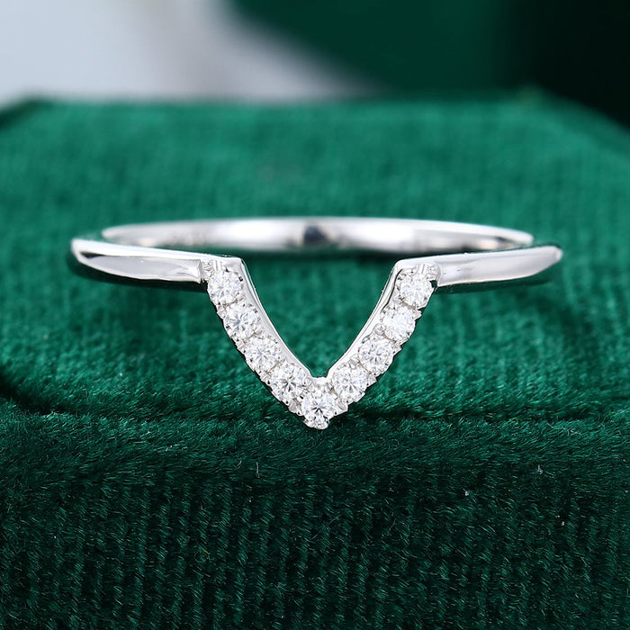 Front view of a V-shaped wedding band with a row of round moissanite stones on green velvet