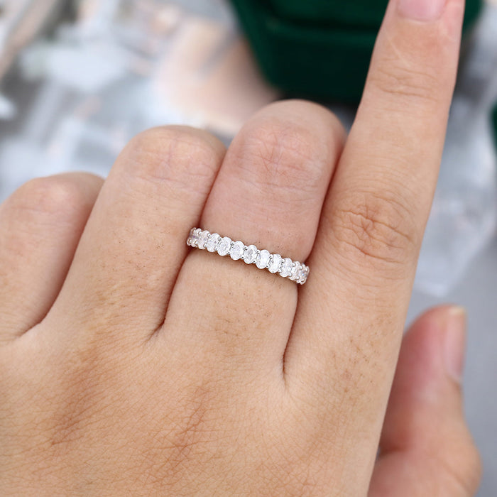 Oval moissanite shared prong half eternity wedding band in white gold worn on the finger