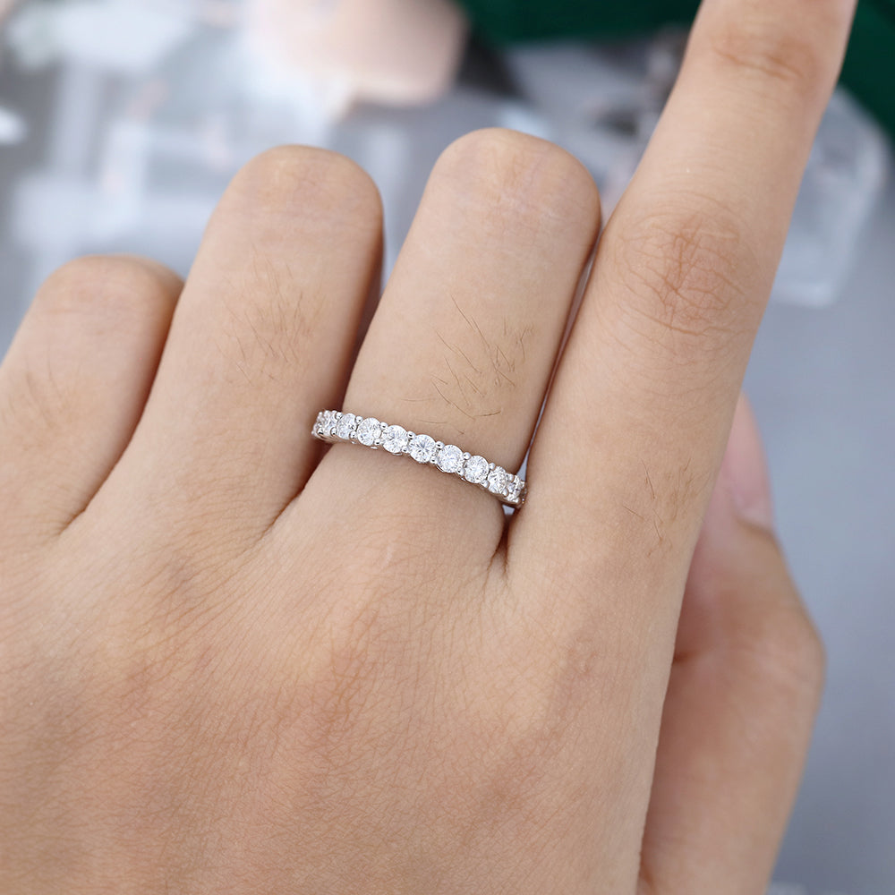 Round moissanite shared prong half eternity wedding band in white gold worn on the finger