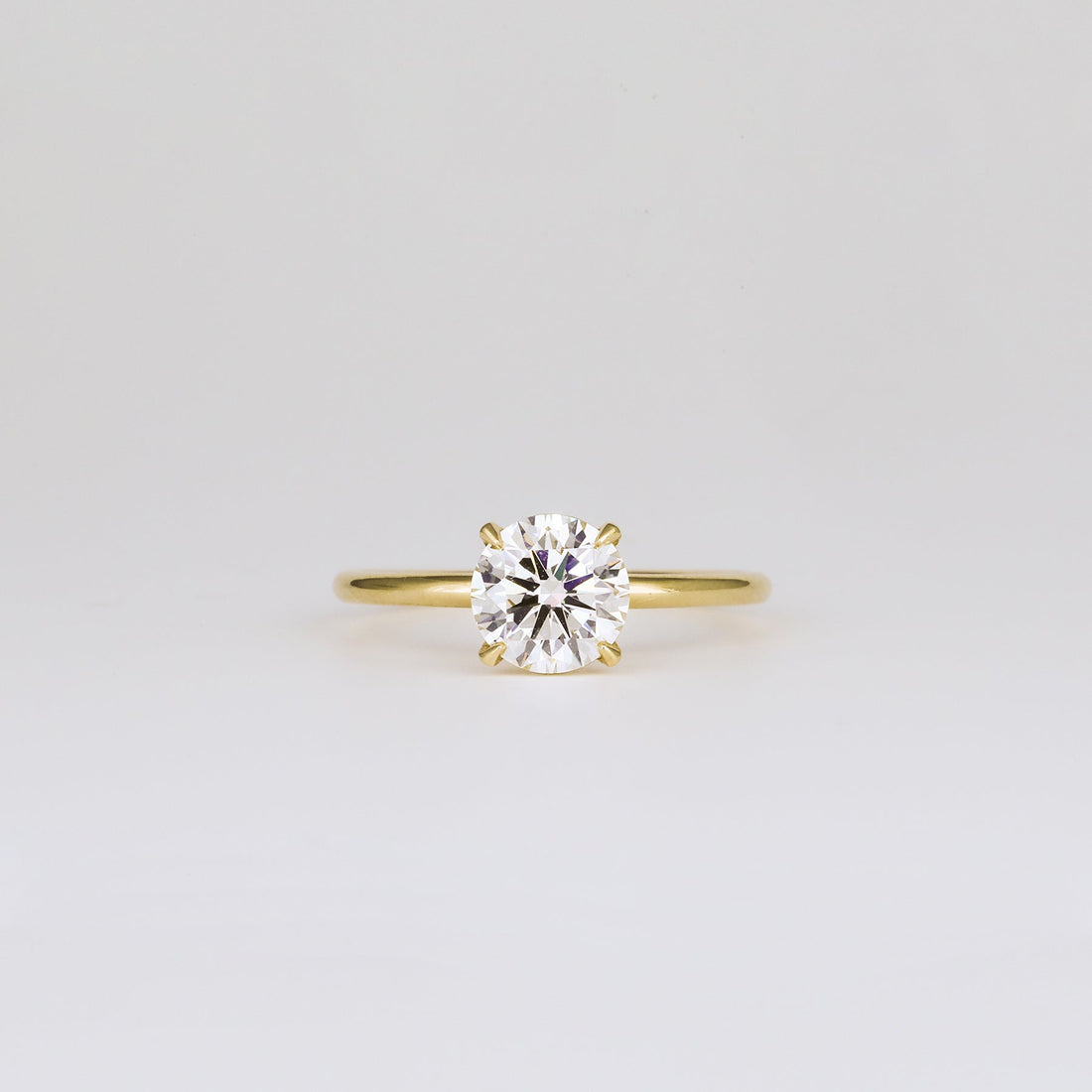 Round cut lab grown diamond four claw solitaire ring on a thin band in yellow gold