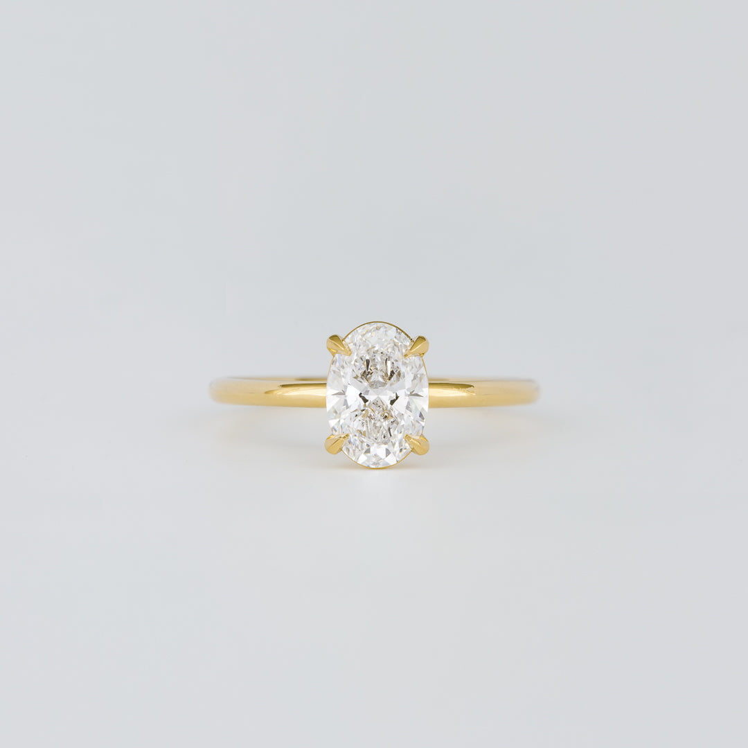 Oval cut lab grown diamond four claw solitaire ring on a thin band in yellow gold