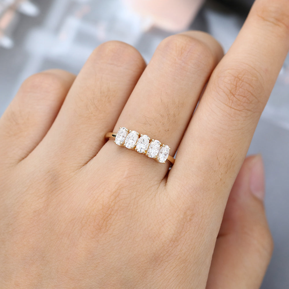 Oval moissanite five stone wedding band in yellow gold worn on the finger