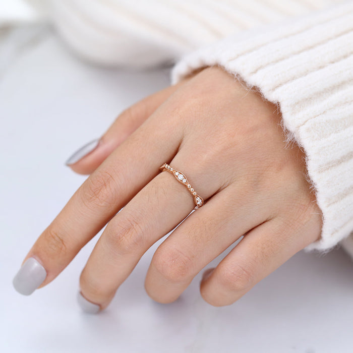 Rose gold vintage beaded moissanite wedding band worn on a finger next to a cream sweater