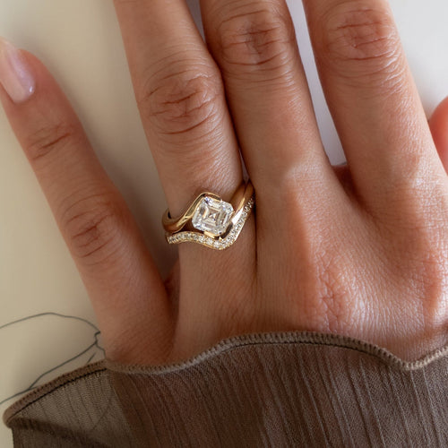 Asscher moissanite swirl bridal set with pave contour band in yellow gold worn on the hand