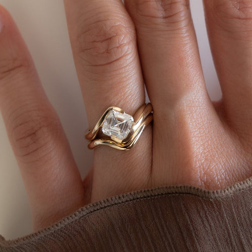 Asscher moissanite swirl bridal set with plain contour band in yellow gold worn on the hand