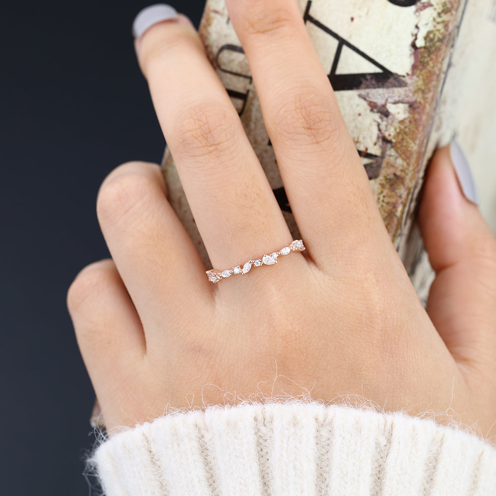 Rose gold scattered multi stone moissanite band worn on a finger holding a book