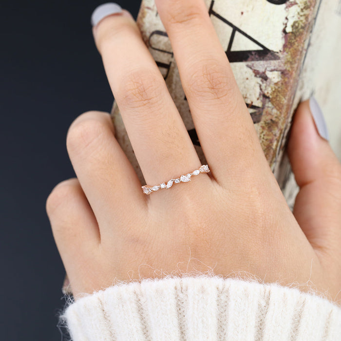 Rose gold scattered multi stone moissanite band worn on a finger holding a book
