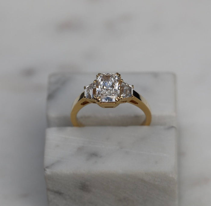 Radiant cut lab grown diamond three stone ring with trapezoid step cut sides in yellow gold