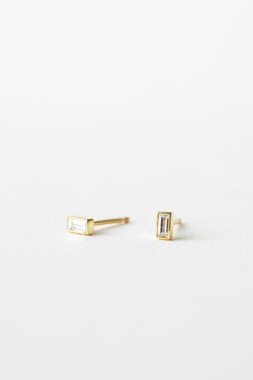 Pair of small yellow gold bezel set baguette lab grown diamond stud earrings on a white background