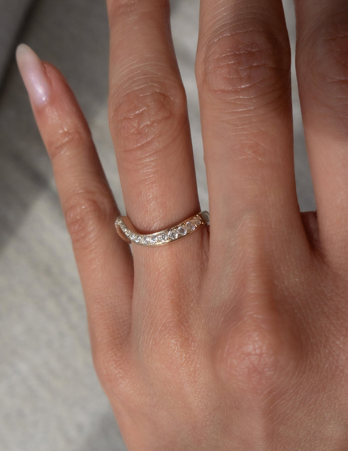 Close view of a curved wave pave wedding band with round moissanite on the ring finger