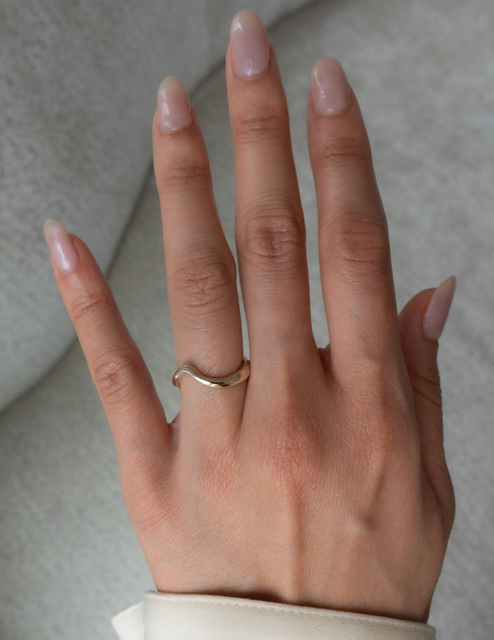 Polished plain contour wedding band in gold worn on the ring finger