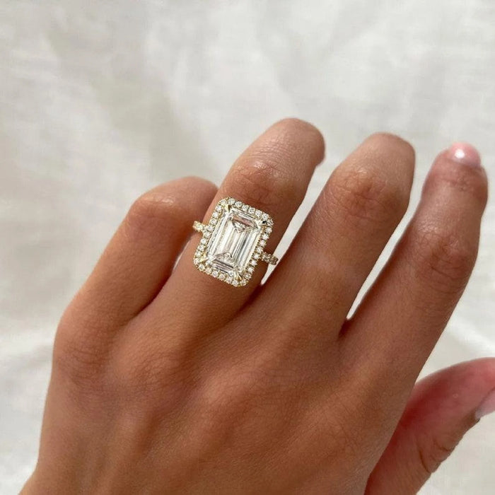 Rectangular halo of round accents around the emerald cut centre stone