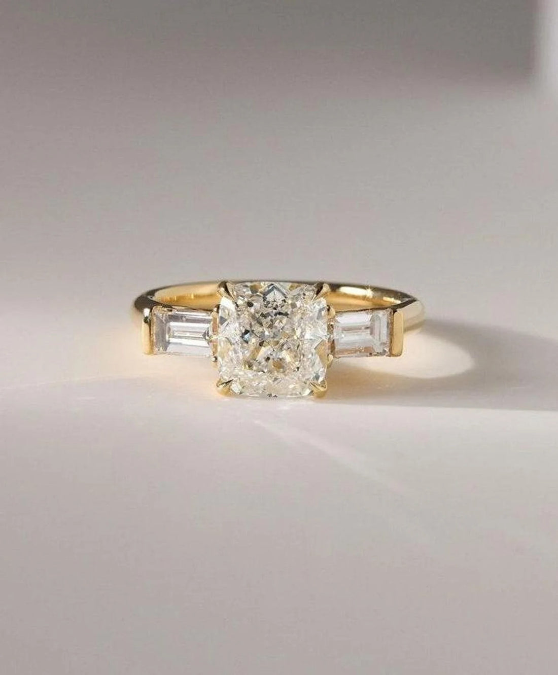 Cushion cut lab grown diamond three stone engagement ring with tapered baguettes in yellow gold