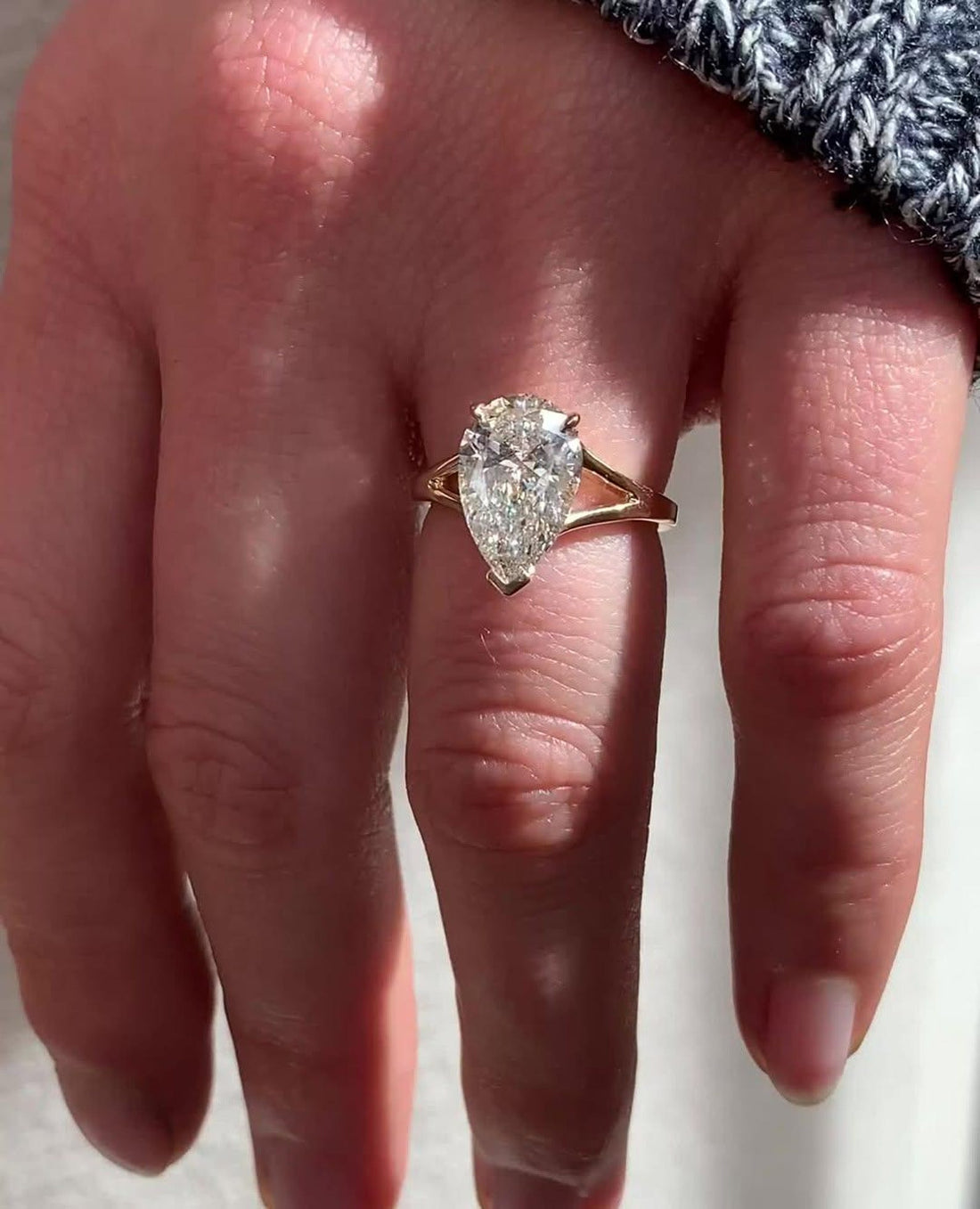 Pear cut lab grown diamond solitaire engagement ring on a split shank in yellow gold, worn on the hand
