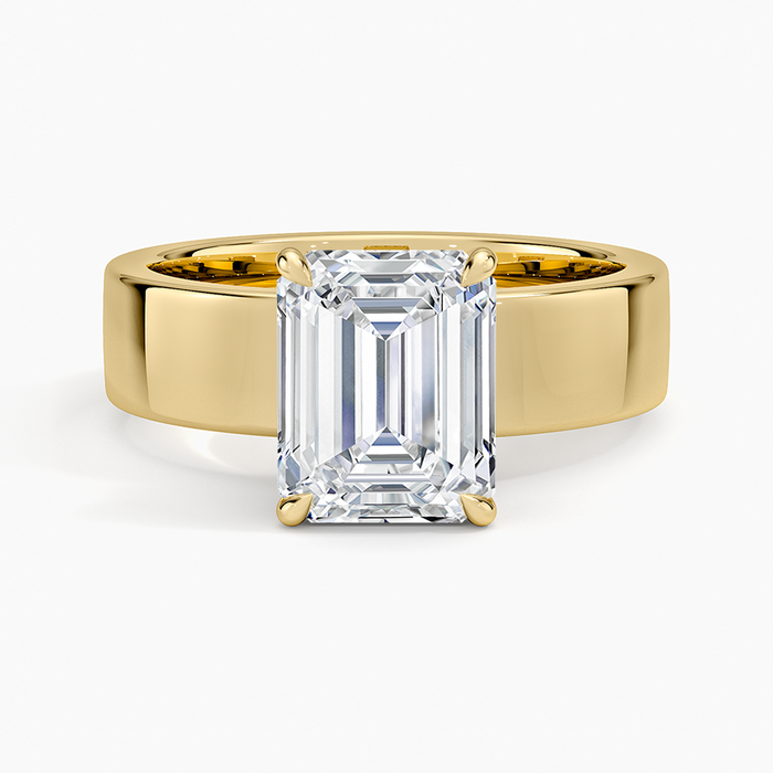 Emerald cut lab grown diamond ring in yellow gold raised above a wide flat band, top view