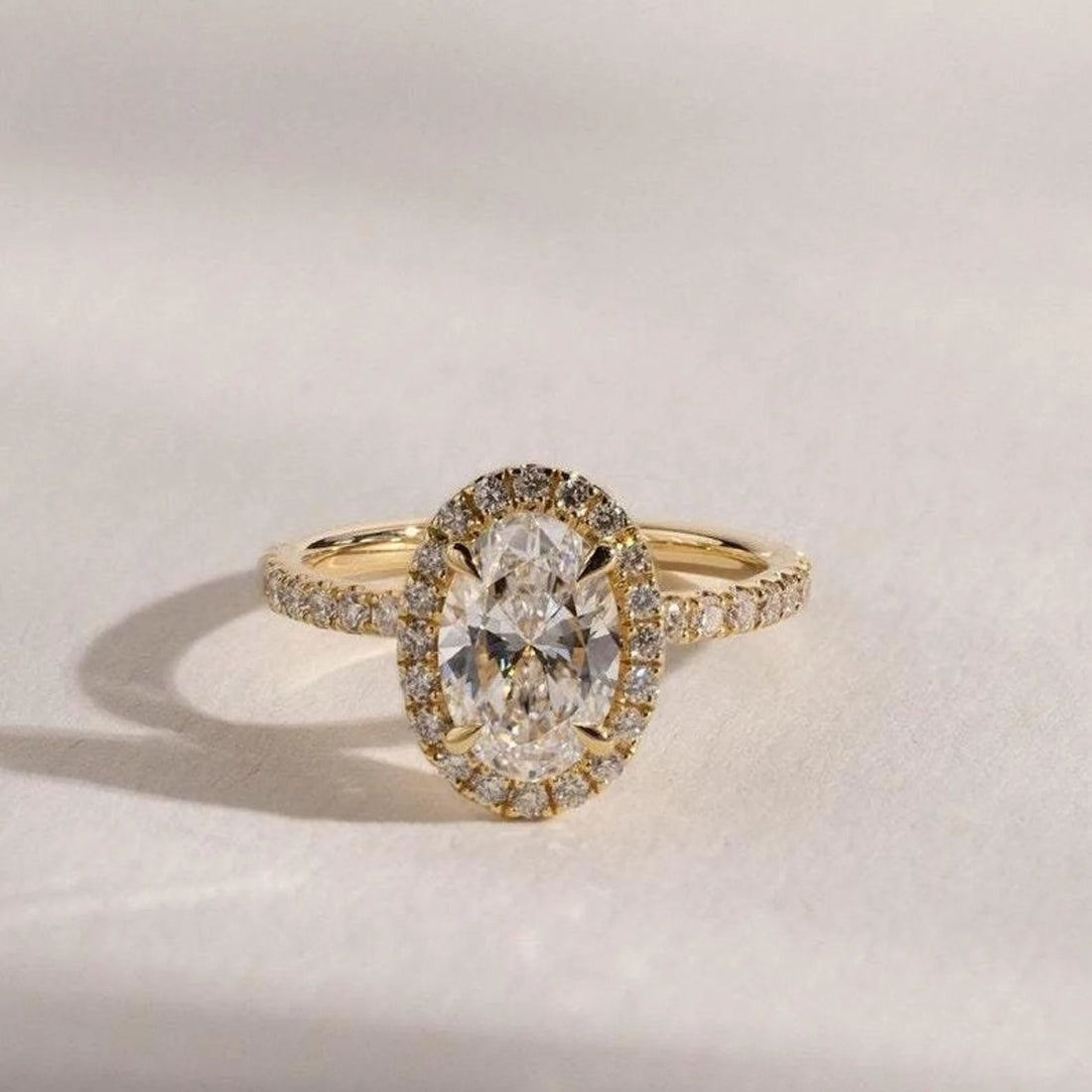 Oval cut lab grown diamond halo engagement ring with pave band in yellow gold