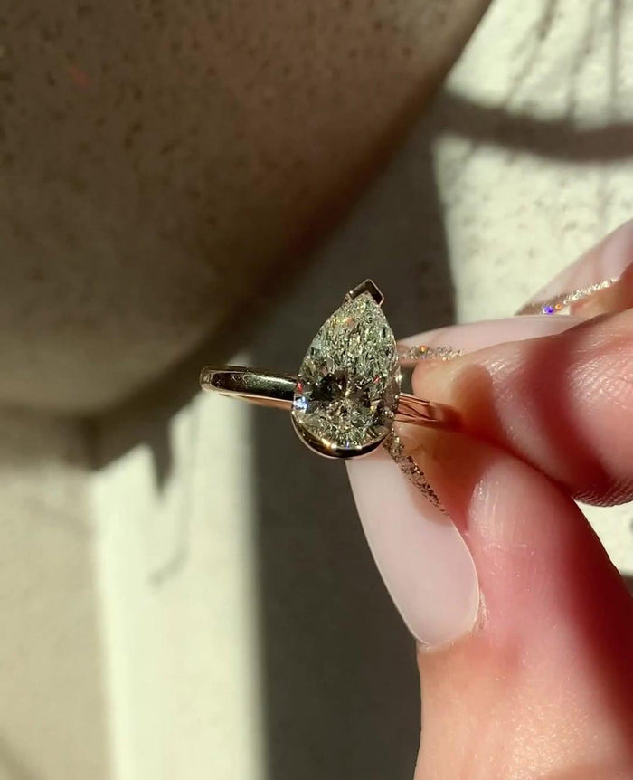 Half bezel rails wrapping the long sides of the elongated pear diamond