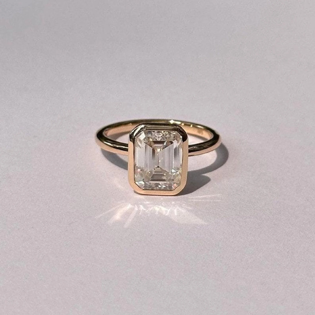 Bezel set emerald cut lab grown diamond solitaire engagement ring on a fine band