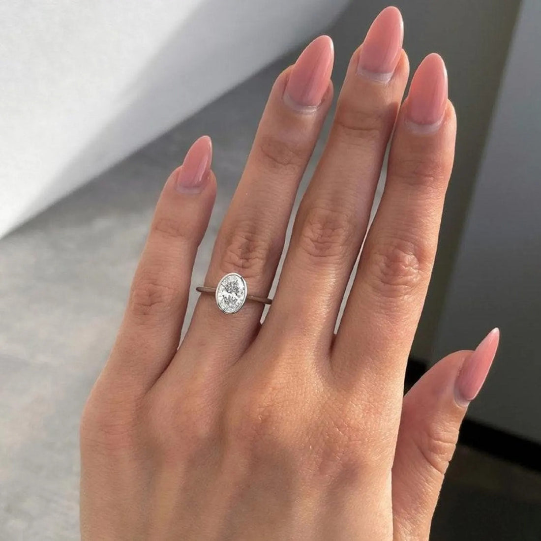 Bezel set oval cut lab grown diamond solitaire engagement ring shown on the hand