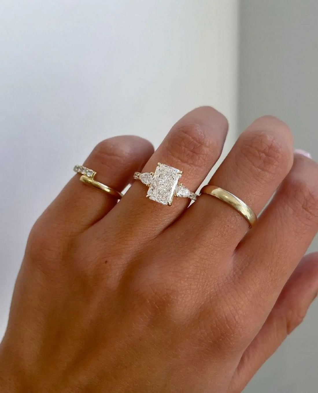 Three stone radiant cut lab grown diamond engagement ring with pear side stones in yellow gold