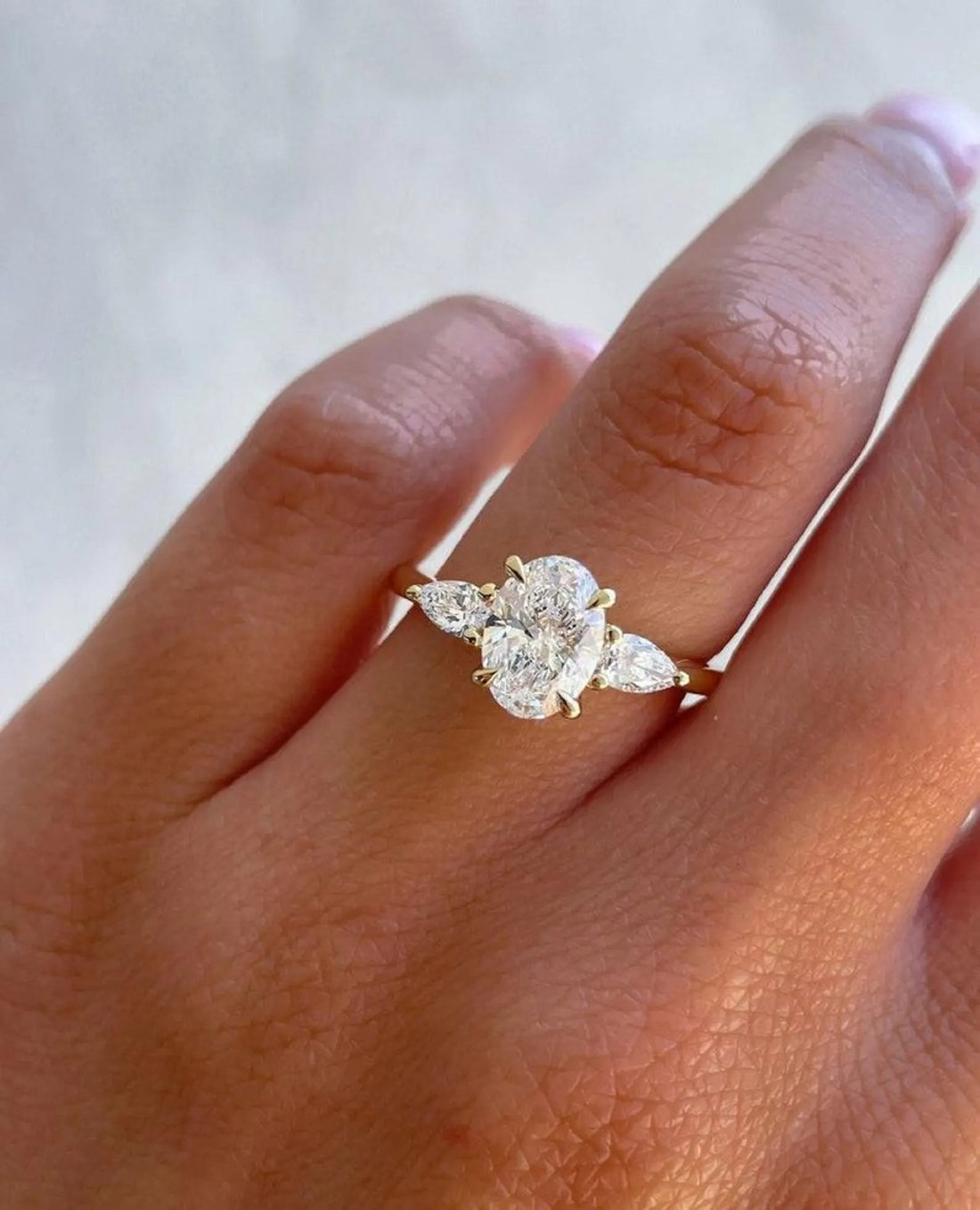 Three stone oval cut lab grown diamond engagement ring with pear side stones in yellow gold